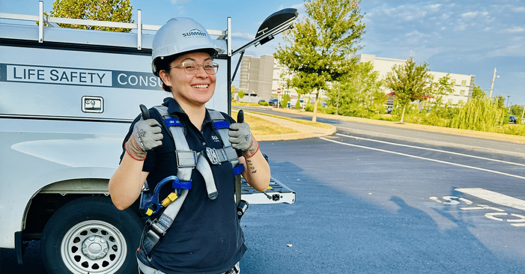 Yensi Morales wearing a harness next to a Summit Fire & Security company truck